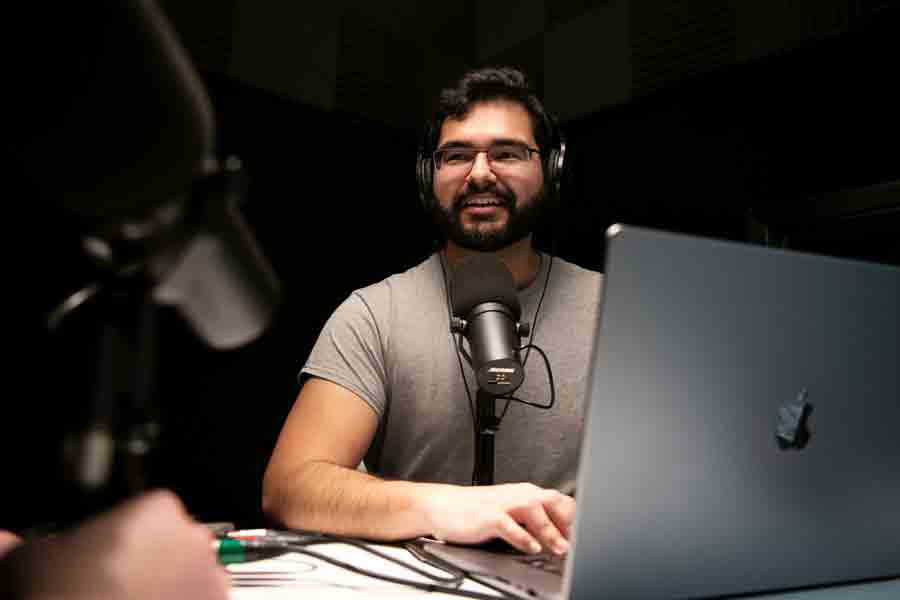 A Drake journalism student records a podcast, using a microphone and laptop in a campus recording studio