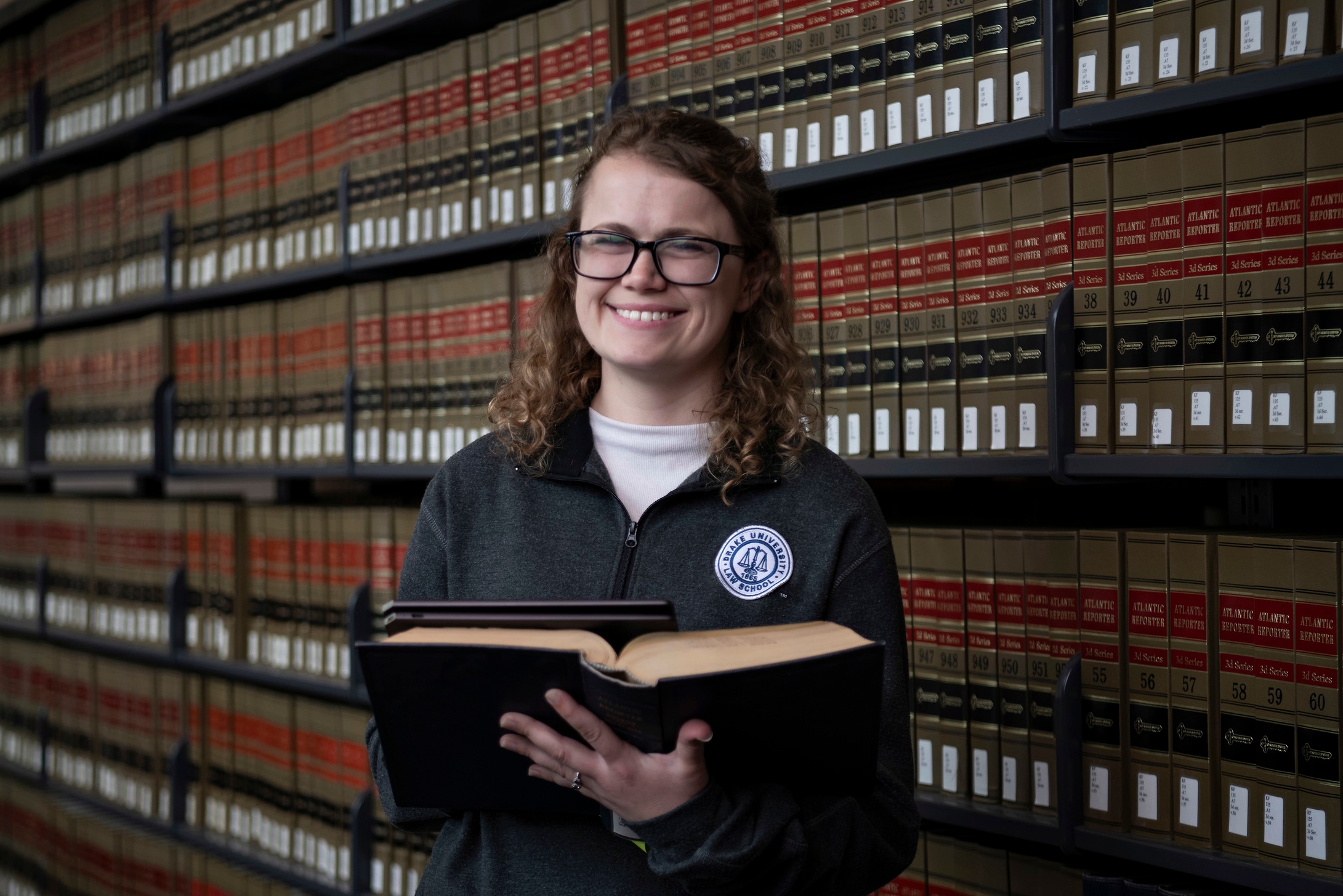 A student in Drake's Journalism/Law 3+3 Law program holds a book while smiling in a law library