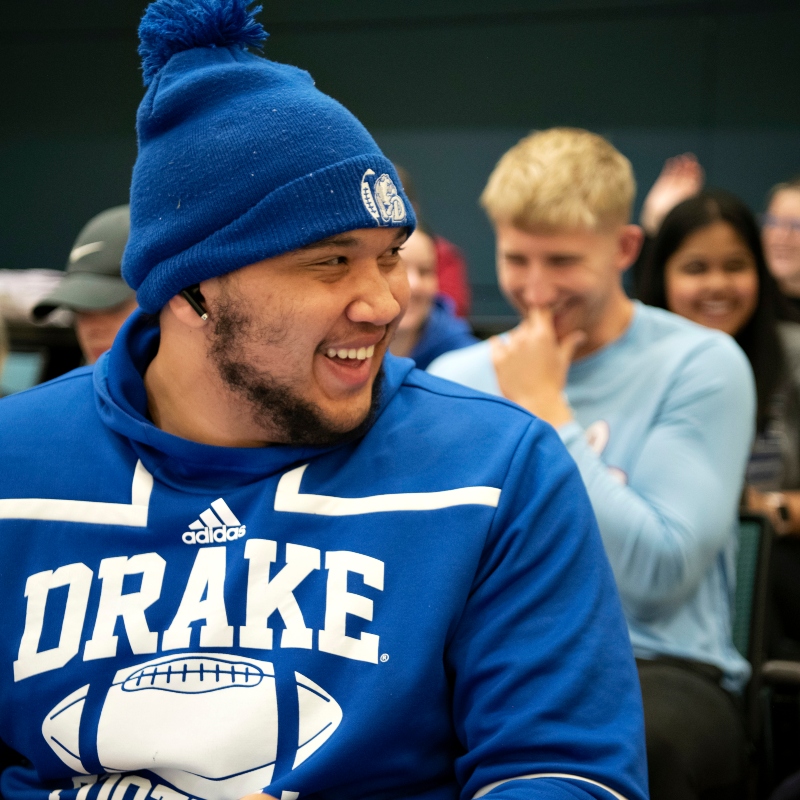 A Drake student wearing a school sweatshirt and hat looks over their shoulder in a campus lecture hall