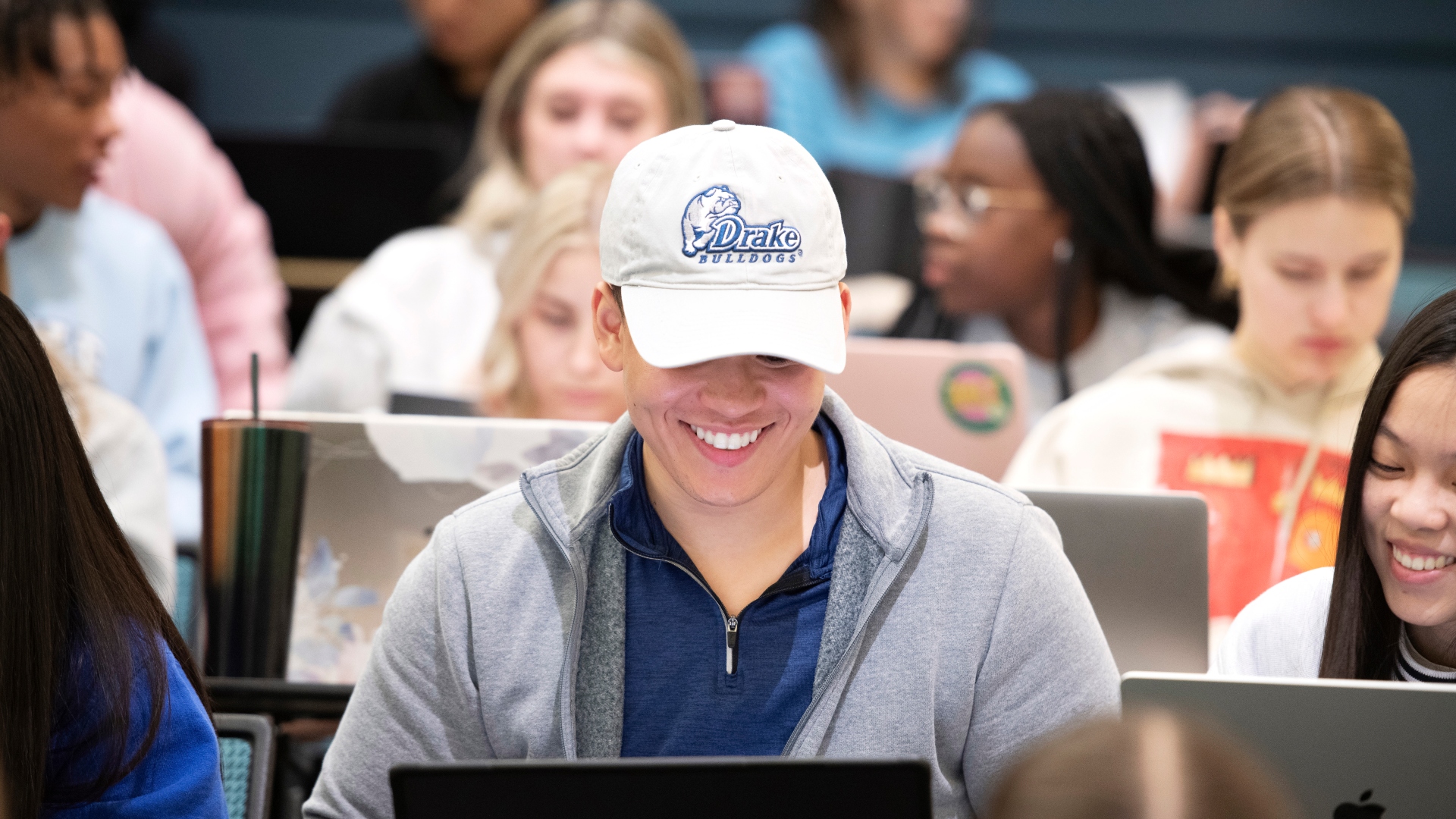 Wearing a school ball cap, a student enrolled in one of Drake's 3 to a Health Sciences Degree and Joint Programs looks down at their laptop to review course notes
