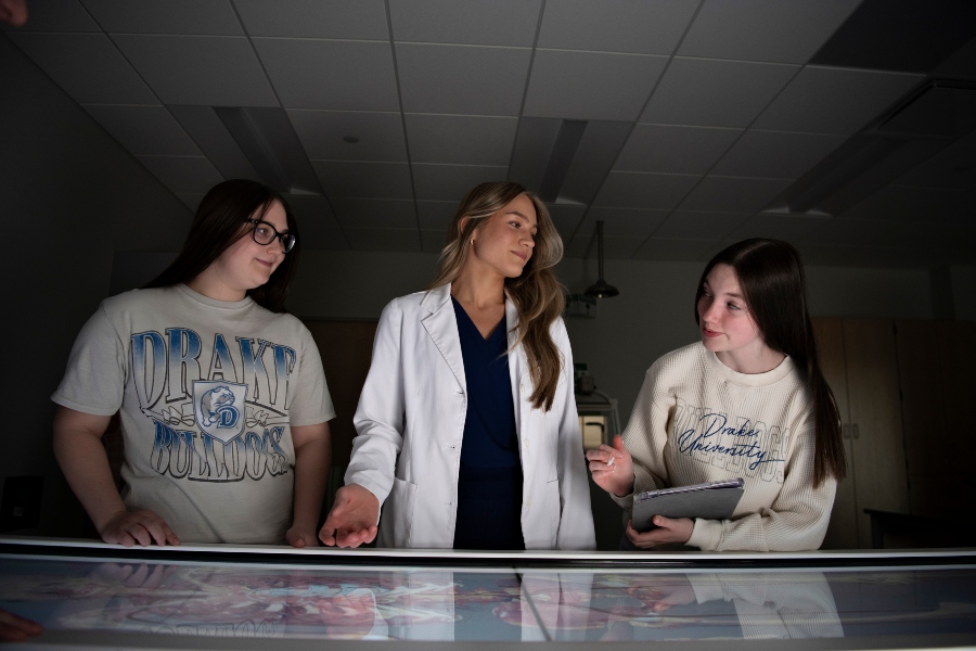 Using a lit anatomage table, an instructor wearing a lab coat explains systems of the human body to two students enrolled in Drake's 3 to a Health Sciences Degree and Joint Programs