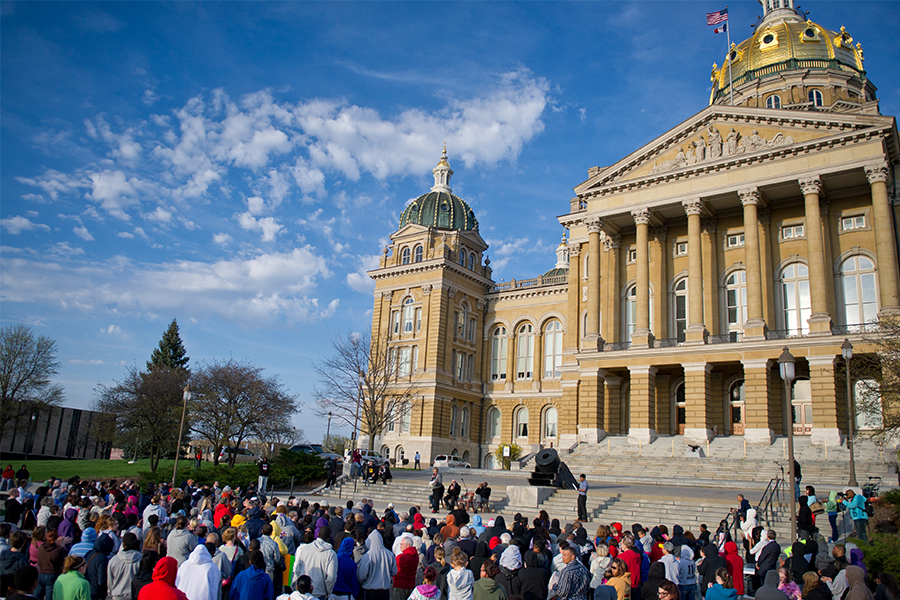 A crowd of people, including Drake students, listens to a speaker outside the Iowa State Capitol building