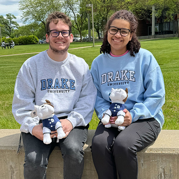 Two students sitting on a concrete bench wearing Drake apparel and holding stuffed Drake Bulldogs.