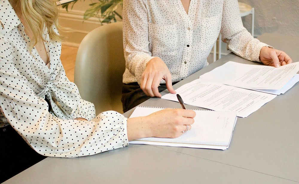 Decorative - Two women sitting at a table pointing at paperwork.