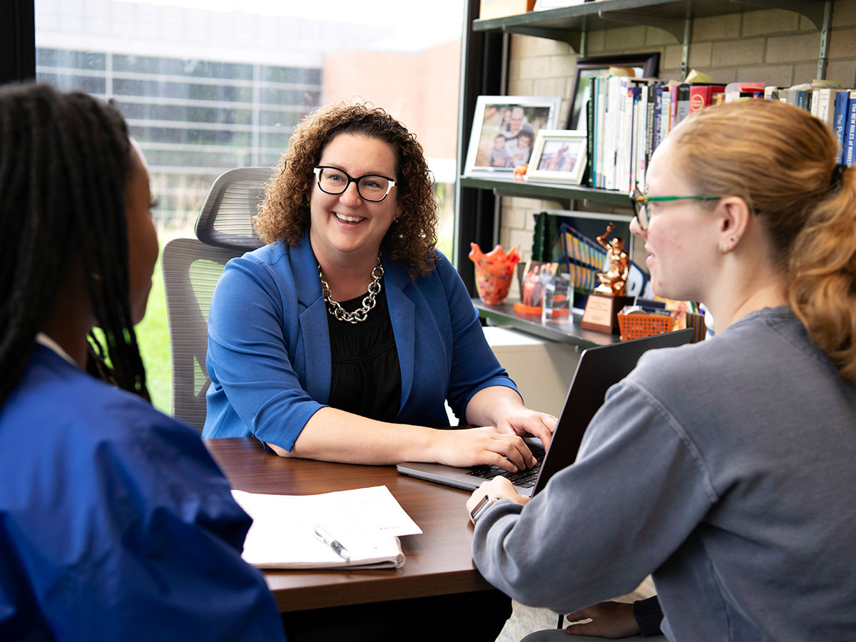 Dean Kelly Bruhn talking with two students in her office.